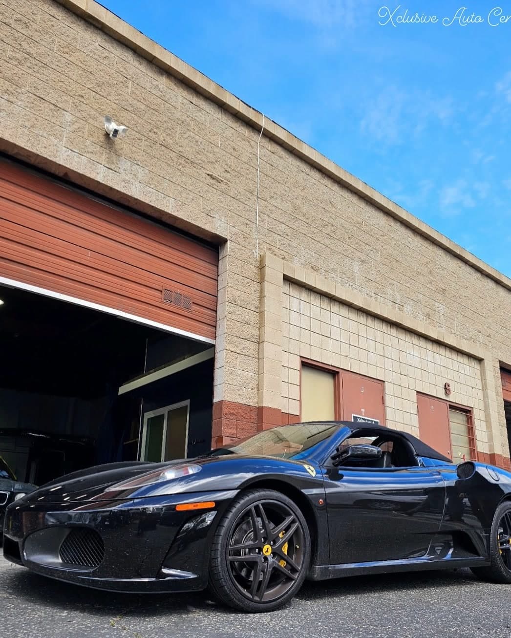 A black Ferrari parked in front of the shop's bays